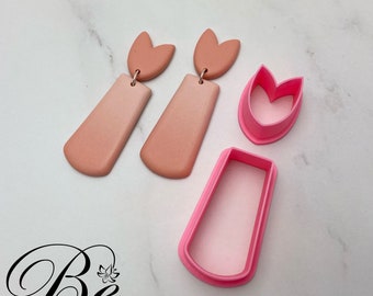 May include: A set of three pink polymer clay earring cutters. The cutters are shaped like a tulip, a rectangle, and a teardrop. The cutters are used to create earrings from polymer clay.