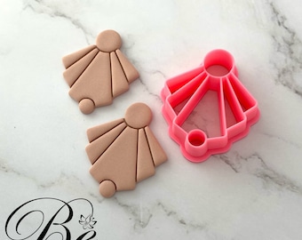 May include: Two pink clay earrings in the shape of a sunburst with a small circle in the center. A pink plastic cookie cutter in the shape of a sunburst is also shown.