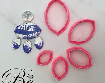 May include: Five pink plastic cookie cutters shaped like elongated leaves. The cutters are arranged in a circle on a white surface.