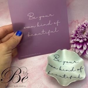 May include: A white ceramic dish with a wavy edge and the text "Be your own kind of beautiful" in black lettering. The dish is sitting on a pink surface.
