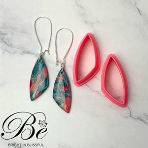 Puede incluir: Un par de pendientes colgantes con un diseño marmoleado en azul verdoso, rosa y blanco. Los pendientes están hechos de arcilla polimérica y tienen ganchos plateados. La imagen también muestra el molde utilizado para crear los pendientes.