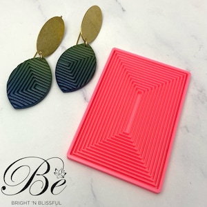 May include: A pink silicone mould with a rectangular shape and multiple concentric squares. The mould is designed for creating layered polymer clay earrings. Two green and blue gradient polymer clay earrings with gold accents are shown next to the mould.