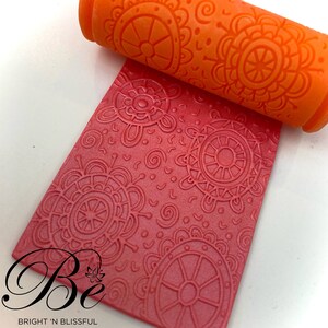 May include: A red and orange silicone rolling pin with a mandala design. The rolling pin is used to create decorative patterns on fondant or clay.
