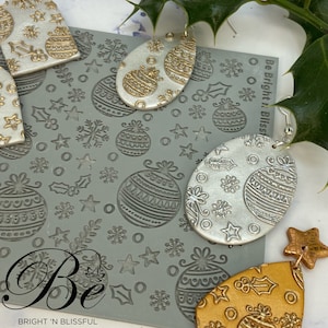 May include: A set of three polymer clay earrings featuring a Christmas ornament design. The earrings are in gold, silver, and yellow with a textured surface. The earrings are displayed on a gray background with a Christmas ornament design.