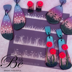 Puede incluir: Un conjunto de cuatro pendientes de arcilla polimérica con un diseño degradado. Los pendientes presentan un degradado rosa y morado con puntos blancos y hierba negra. Los pendientes se combinan con pequeños acentos de flores rosas. Los pendientes se muestran sobre un fondo morado con una plantilla de hierba y flores.