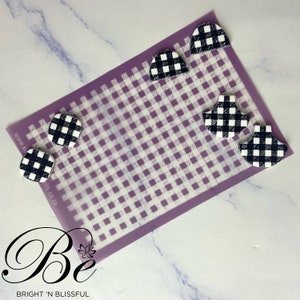 May include: A sheet of clear plastic with a black and white gingham pattern printed on it. There are five black and white gingham shapes on the sheet, including two squares and three half circles.