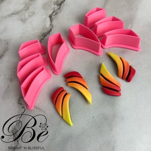 May include: Pink plastic cookie cutters shaped like a curved wing, a flower, and a set of stacked arches. Three polymer clay earrings are shown in the image, each with a curved shape and a gradient of red, orange, and yellow.