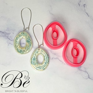 May include: A pair of green and white ceramic earrings with a ring design. The earrings are shown next to two pink plastic moulds.