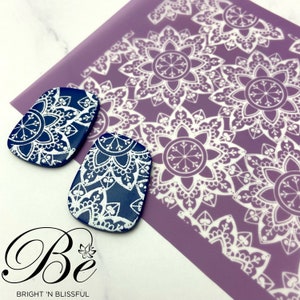 May include: Two blue and white ceramic earrings with a mandala design. The earrings are on a purple background with a white mandala pattern.