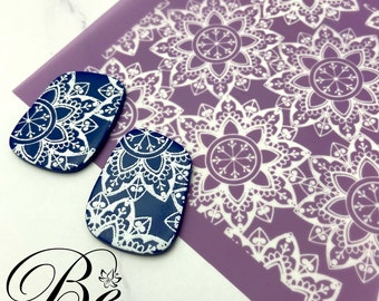 May include: Two blue and white ceramic earrings with a mandala design. The earrings are on a purple background with a white mandala pattern.
