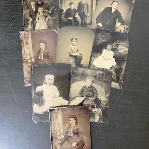 May include: A collection of antique photographs, featuring portraits of individuals and groups. The images are in black and white, with varying sizes and shapes. Some photos show people in formal attire, while others depict children. The photographs are arranged on a dark surface.
