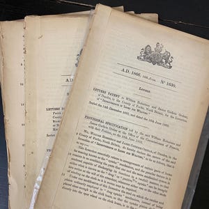 May include: Antique documents from 1866, featuring text and a coat of arms. The papers are aged with visible wear and tear, and are sealed in a clear plastic sleeve. The documents are related to looms and weaving.