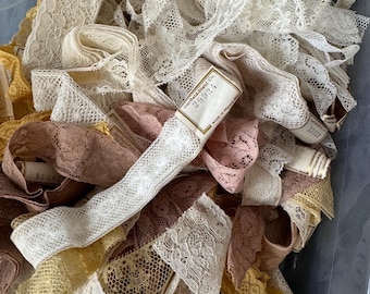 May include: A large bin filled with various colors of lace trim. The lace is delicate and intricate, with a variety of patterns. The lace is in a variety of colors, including white, cream, pink, and yellow. The lace is in a variety of widths, and some of the lace has a label that reads "Charles Redd & Co. 28934".