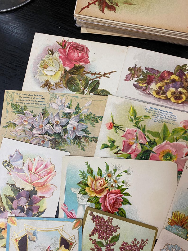 Puede incluir: Una colecci&oacute;n de postales florales vintage con rosas, pensamientos y otras flores en varios colores. Algunas tarjetas tienen texto, incluyendo citas y poemas. Las tarjetas est&aacute;n dispuestas sobre una superficie oscura.