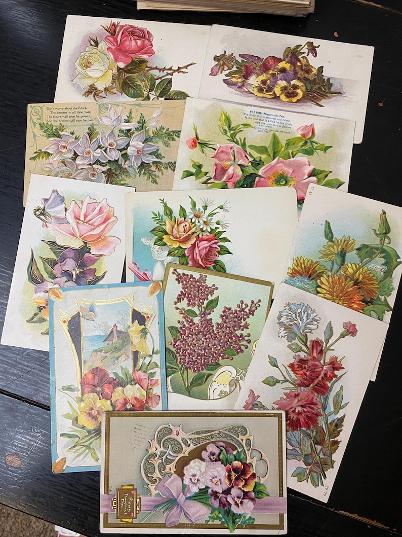 Puede incluir: Una colecci&oacute;n de postales florales vintage. Las postales presentan varios arreglos florales, incluyendo rosas, pensamientos y lilas, en tonos rosa, amarillo, morado y rojo. Algunas tarjetas tienen bordes decorativos y texto.