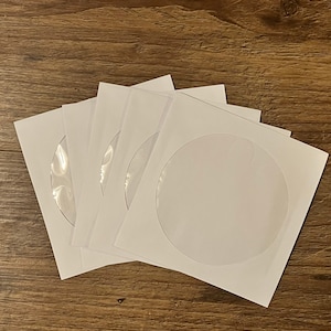 Peut inclure: Cinq pochettes blanches pour CD avec fenêtres en plastique transparent pour ranger des CD ou des DVD.