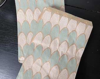 May include: A stack of brown paper gift bags with a teal and gold geometric pattern. The bags are folded and ready to be used.