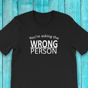 Può includere: Maglietta nera con testo bianco che dice "You're asking the WRONG PERSON".