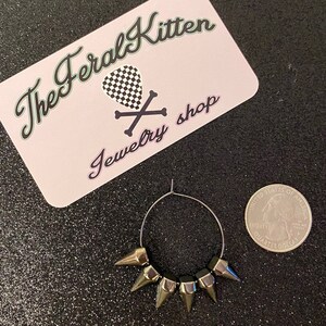 May include: Silver hoop earrings with five silver spikes. The earrings are about the size of a US quarter.