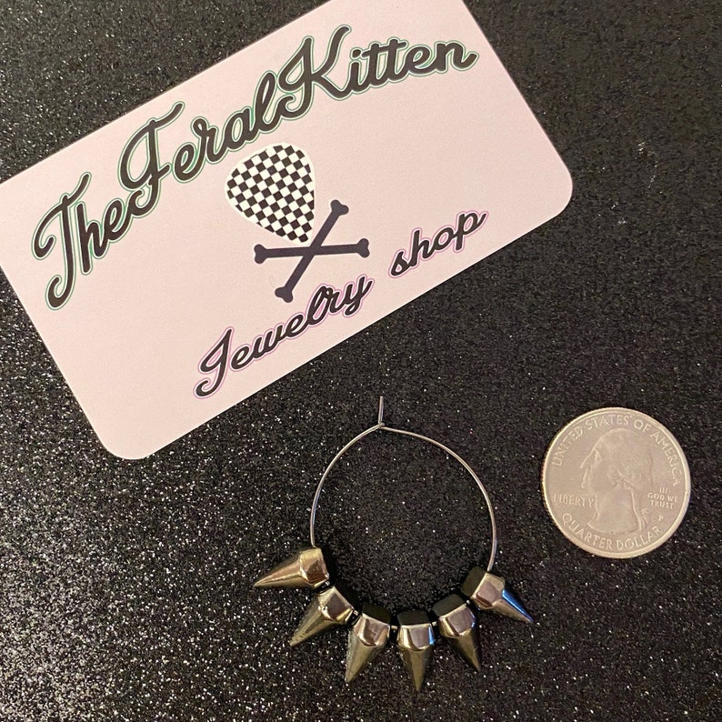 May include: Silver hoop earrings with five silver spikes. The earrings are about the size of a US quarter.