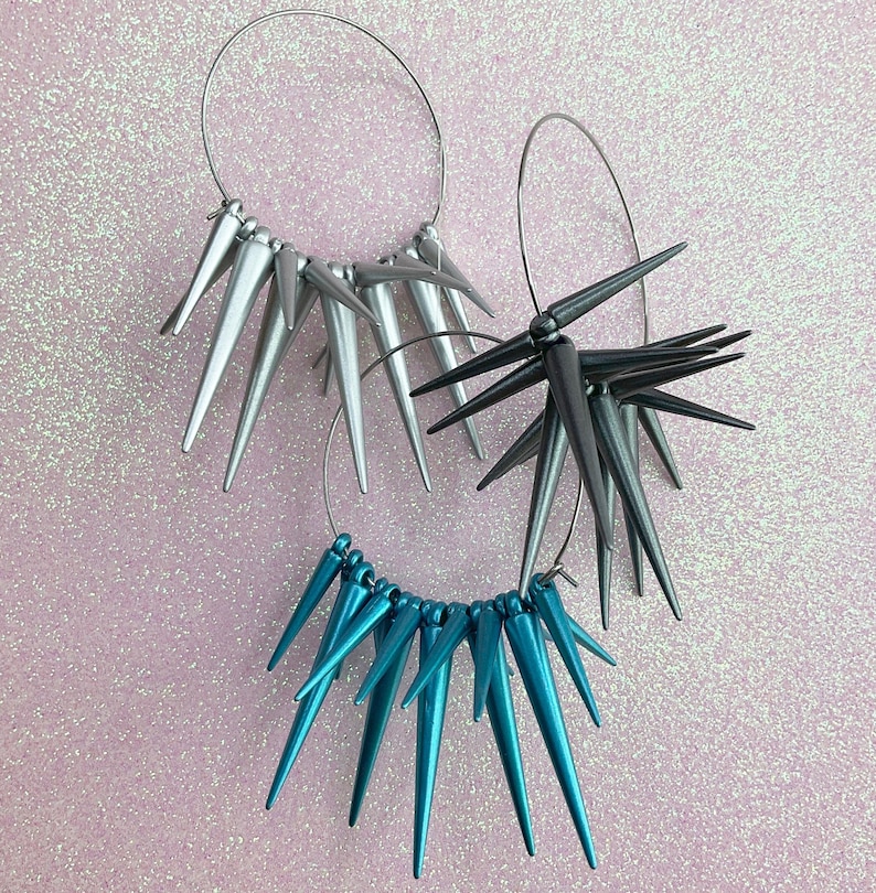 May include: Three pairs of hoop earrings with spikes. The earrings are silver, black, and teal.
