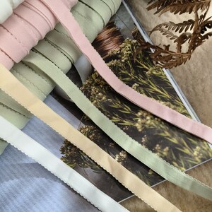 May include: Five different colors of satin ribbon with scalloped edges. The colors are white, light pink, light green, beige, and light blue.