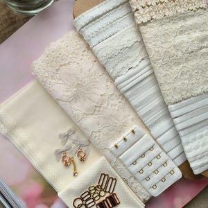 Puede incluir: Surtido de encajes blancos, elásticos y cierres de sujetador. También hay cierres metálicos dorados y piezas decorativas.