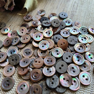May include: A large pile of brown and iridescent shell buttons with two holes each. Some buttons are made of wood with a dark brown grain.