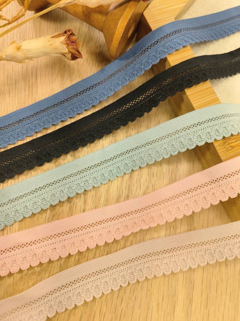 May include: Four different colors of elastic lace trim with scalloped edges. The colors are blue, black, light blue, and pink.