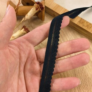 May include: Black elastic trim with a delicate lace pattern. The trim is approximately 1 inch wide and has a scalloped edge.
