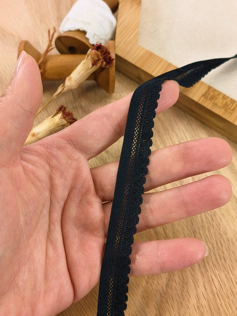 May include: Black elastic trim with a delicate lace pattern. The trim is approximately 1 inch wide and has a scalloped edge.