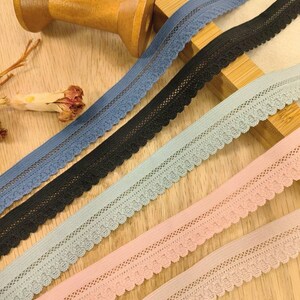 May include: Five spools of elastic lace trim in different colors: blue, black, light blue, pink, and a lighter shade of pink. The lace trim has a scalloped edge and a delicate floral pattern.