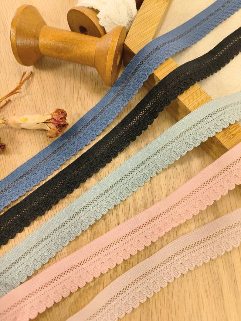 May include: Five spools of elastic lace trim in different colors: blue, black, light blue, pink, and a lighter shade of pink. The lace trim has a scalloped edge and a delicate floral pattern.