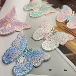 May include: Five embroidered butterfly patches in various pastel colors, including pink, blue, and green. The butterflies are on a white background.