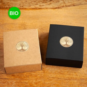Könnte beinhalten: Zwei Schachteln mit einem Lebensbaum-Design. Eine Schachtel ist braun mit dem Wort "BIO" auf einem grünen Aufkleber. Die andere Schachtel ist schwarz.