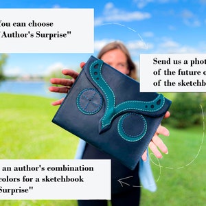 May include: A woman is holding a dark blue leather sketchbook with a green butterfly design. The sketchbook has the text "Author's Surprise" and "Surprise" on it.