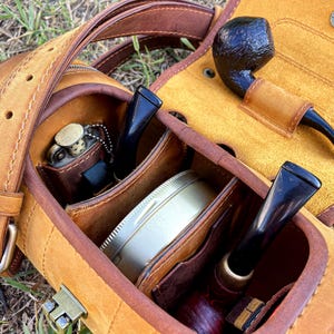 Puede incluir: Una funda de cuero marr&oacute;n para pipa con varios compartimentos para pipas, tabaco y otros accesorios. La funda tiene una correa y una cremallera.