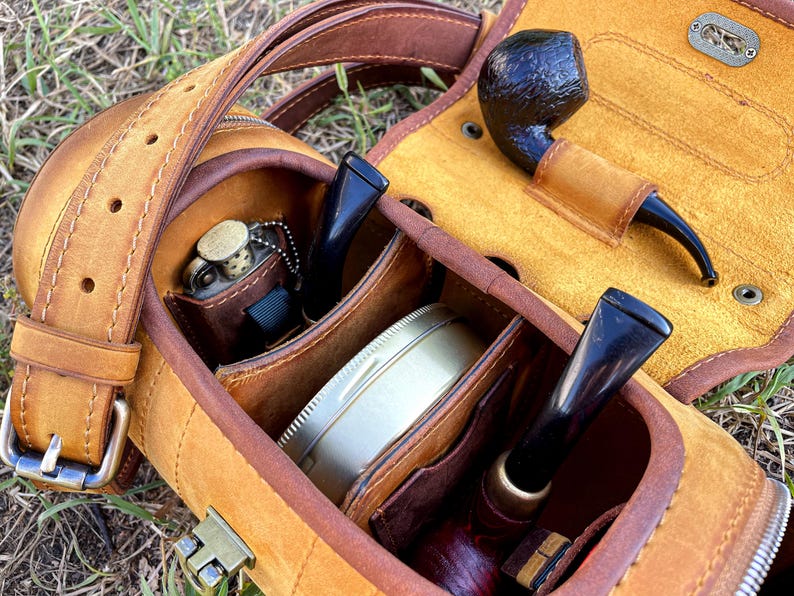Puede incluir: Una funda de cuero marr&oacute;n para pipa con varios compartimentos para pipas, tabaco y otros accesorios. La funda tiene una correa y una cremallera.