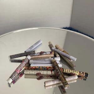 May include: A collection of rolled up paper scrolls with various patterns and text. The scrolls are scattered on a reflective surface.