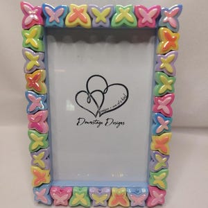 May include: A light blue picture frame with a colorful butterfly design. The frame is decorated with pastel-colored butterflies, each with a different color and pattern. The frame is made of plastic and has a smooth finish. The frame is 4x6 inches in size. The frame is perfect for displaying photos, artwork, or other small items.
