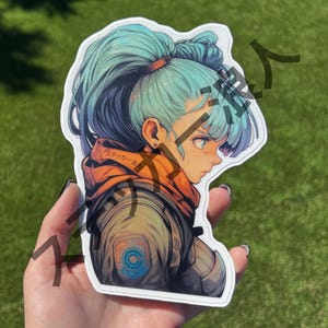 May include: A sticker featuring a side profile of a character with teal hair in a high ponytail. The character wears an orange hooded jacket over a gray jacket with a blue emblem. The sticker has a white border and is held against a green background.