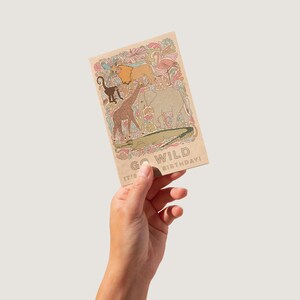 K&ouml;nnte beinhalten: Rechteckige Geburtstagskarte mit braunem Hintergrund und dem Text "GO WILD BIRTHDAY!". Sie zeigt Illustrationen eines L&ouml;wen, Affen, Giraffe, Elefanten und Krokodils. Die Karte hat ein farbenfrohes Blumenmuster.