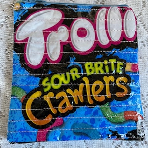 May include: A blue and black zippered pouch with the words "Sour Brite Crawlers" and "Trolli" printed on it. The pouch is made from recycled candy wrappers.
