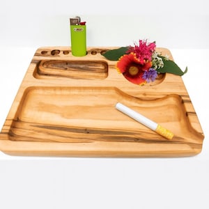 May include: A wooden rolling tray with a lighter, a cigarette, and a small arrangement of flowers. The tray has several carved compartments and a curved edge. The lighter is green, and the cigarette has a yellow filter.