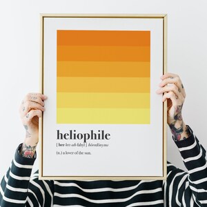 Può includere: Una stampa incorniciata con un design sfumato giallo e arancione. La stampa include la parola "heliophile" e la sua definizione: "[hee-lee-uh-fahyl]  böredönyms (n.) un amante del sole."