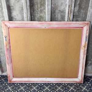 May include: A rectangular picture frame with a distressed pink and white painted finish. The frame features a flat, light brown backing board and includes two metal sawtooth hangers attached to the side rails for wall mounting purposes.