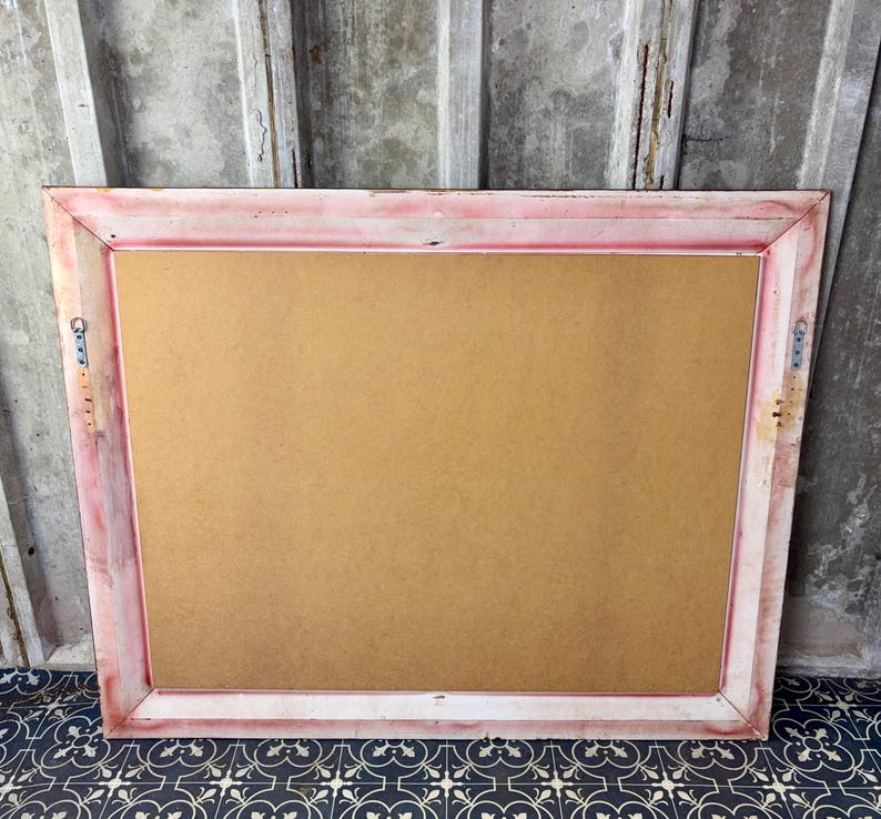 May include: A rectangular picture frame with a distressed pink and white painted finish. The frame features a flat, light brown backing board and includes two metal sawtooth hangers attached to the side rails for wall mounting purposes.