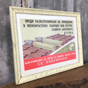 May include: A vintage framed poster with a red and white warning sign in Bulgarian. The poster depicts a diagram of a projectile with the text "ПРЕДИ РАЗПАТРОНИРВАНЕ НА ПРИВЕДЕНИЯ В НЕОКОНЧАТЕЛНО СНАРЯДЕН ВИД ИЗСТРЕЛ, ОТВИНТИ КАПСУЛНАТА ВТУЛКА" and "РАЗПАТРОНИРВАНЕТО НА ИЗСТРЕЛ СЪС ЗАВИНТЕНА КАПСУЛНА ВТУЛКА СЕ ЗАБРАНЯВА".