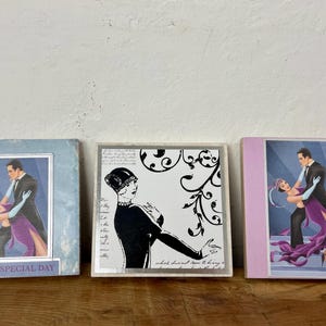 Op de afbeelding: Drie vierkante kunstdrukken met vintage dansillustraties. Eén heeft een blauwe lijst met de tekst "ON YOUR SPECIAL DAY". De andere twee tonen een dansend stel en een vrouw met een hoed.