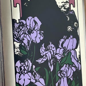 May include: Art Nouveau style print featuring lavender iris flowers with green leaves against a black background. The print has a white border and a decorative top section with a figure.
